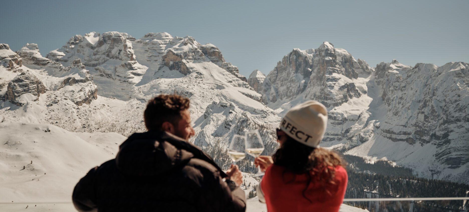 Two friends looking out from a balcony at the snowy mountains and blue sky