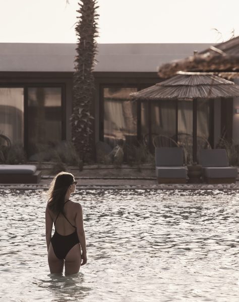 A woman standing in the middle of a beautiful lagoon at Casa Cook North Coast in a black cross back swimming costume and sunglasses