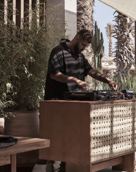 A DJ working at the Casa Cook North Coast Restaurant, DJ decks are on top of a wood and rattan textured stand with the back ground showing the nature in North Coast