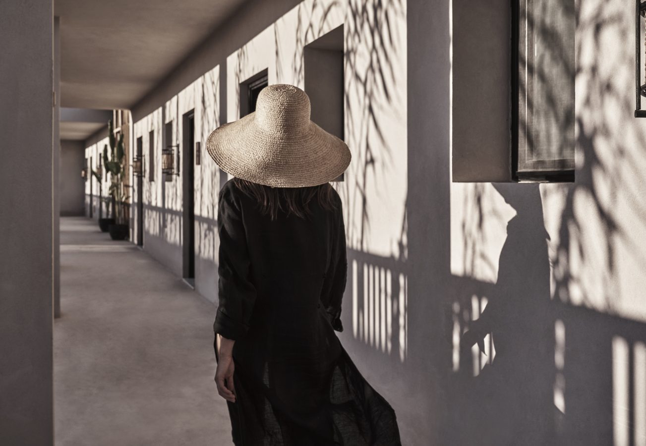 A woman wearing a hat walks confidently through a luxurious hallway, embodying elegance and charm.
