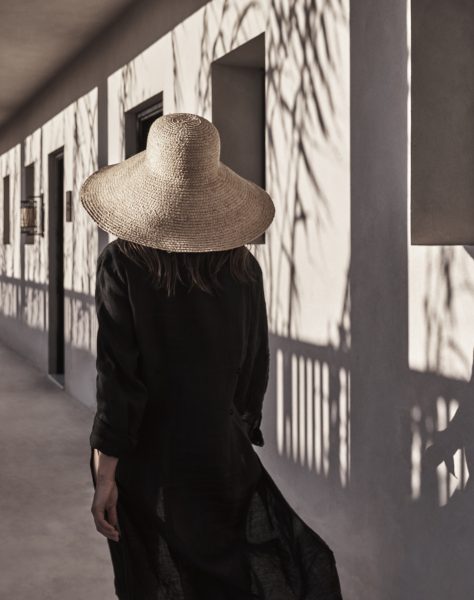A woman wearing a hat walks confidently through a luxurious hallway, embodying elegance and charm.