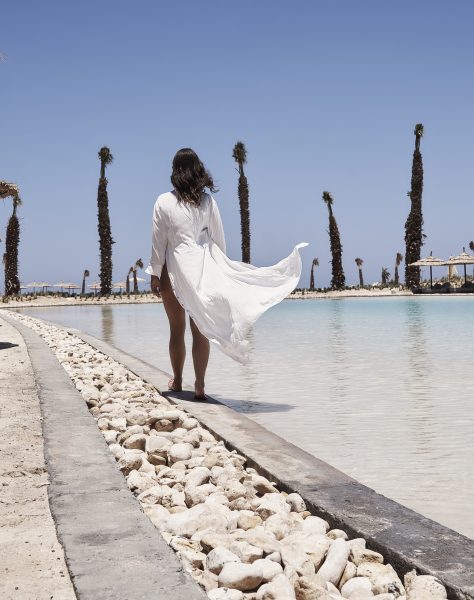 Woman with her back to the camera in a white flowing cover up standing on the edge of a lagoon in Casa Cook North Coast