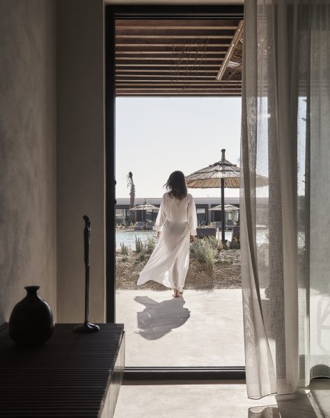 A woman in an elegant white cover up gracefully walks through an open door leading to the serene lagoon at Casa Cook North Coast