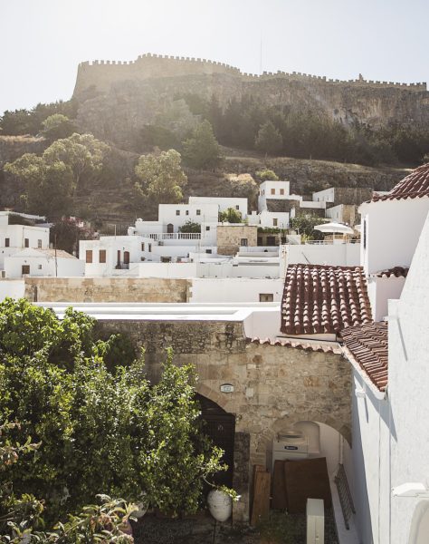 Whitewashed buildings and terracotta rooftops in the traditional village of Lindos with the ancient acropolis rising above, capturing the local charm and cultural essence of Rhodes island near Casa Cook