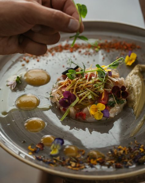 A chef adds microgreens to a vibrant, artfully plated dish at Casa Cook Rhodes, where locally inspired cuisine meets handcrafted presentation in a refined adults-only setting.