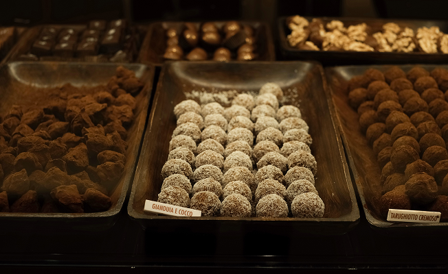 Rows of handcrafted Italian chocolate truffles on display at a local confectionery in Madonna di Campiglio — varieties including gianduja e cocco and tarughiotto cremoso, dusted in cocoa and coconut.