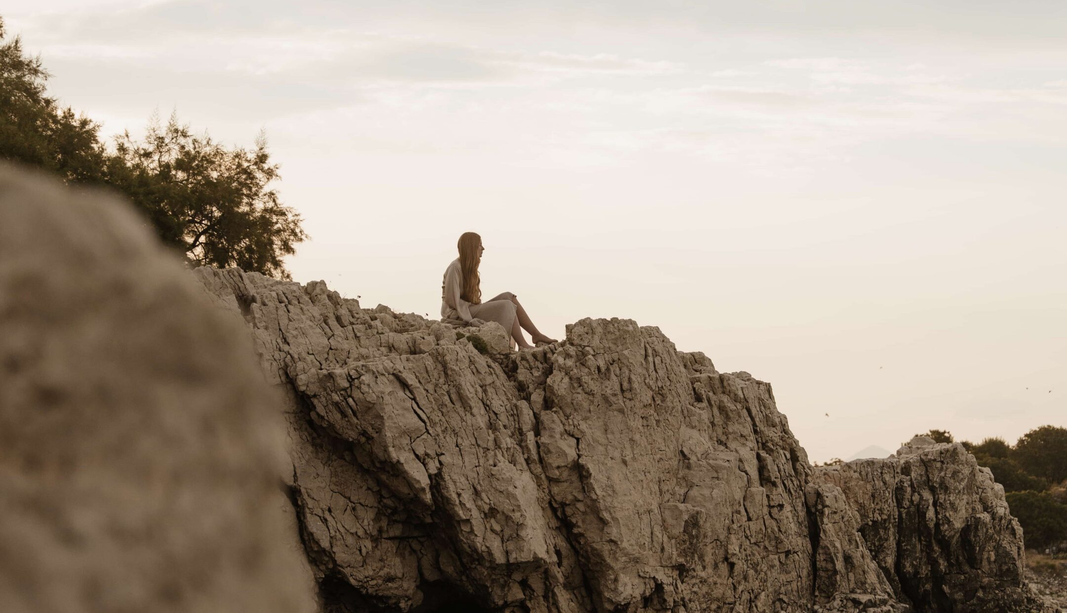 Woman sitting on the top of a big cliff face looking out to the ocean under a clear sky
