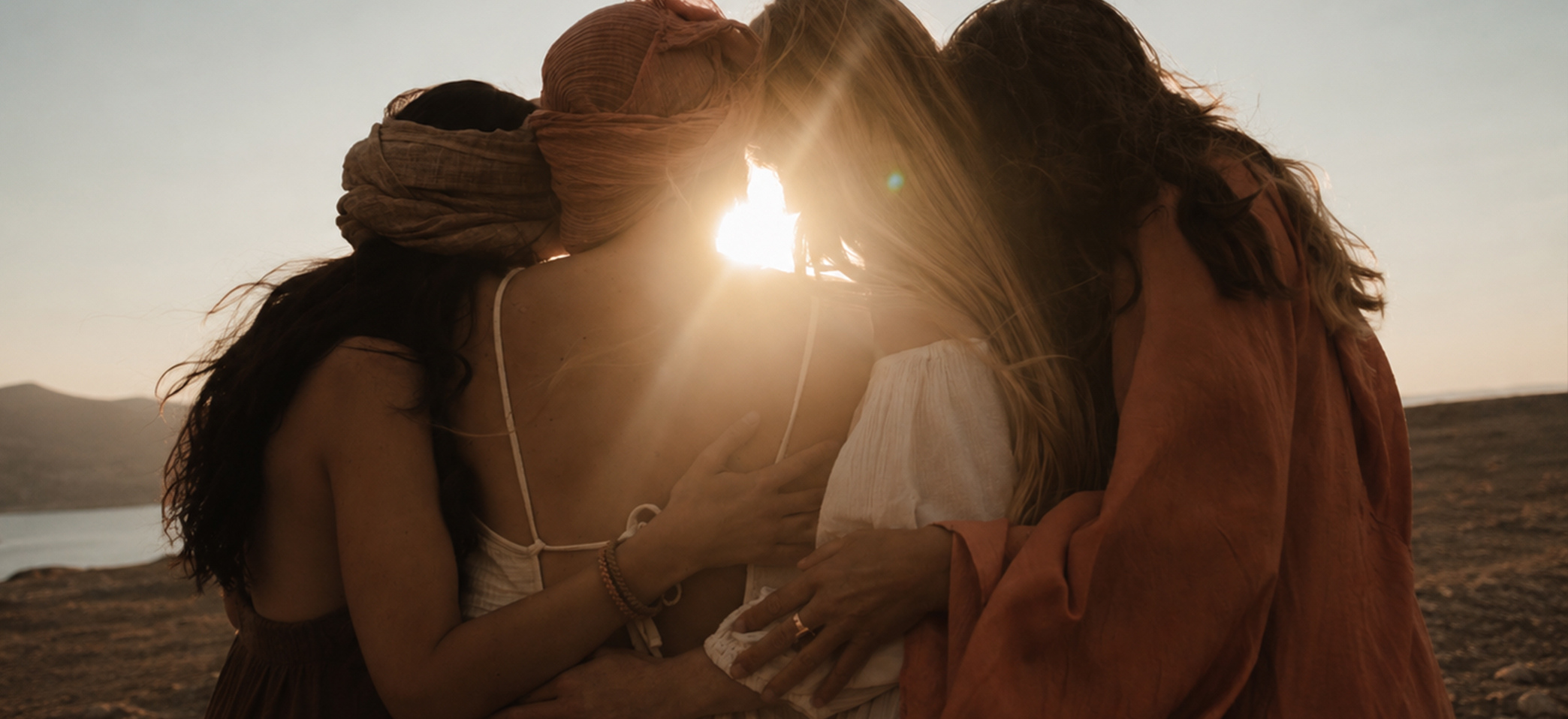 Four women standing together with their arms around each other looking out to the sunset with their backs to the camera