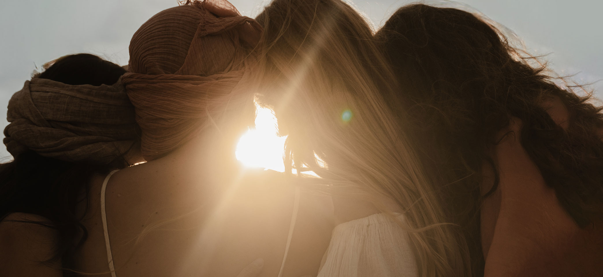 Women leaning their heads together in support looking towards the sun