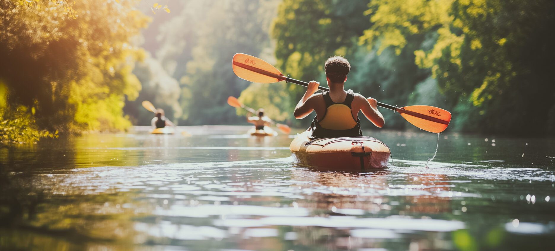 A man in a yellow life jacket paddles a kayak down a river. The scene is peaceful and serene, with the man enjoying the beauty of nature as he navigates the water