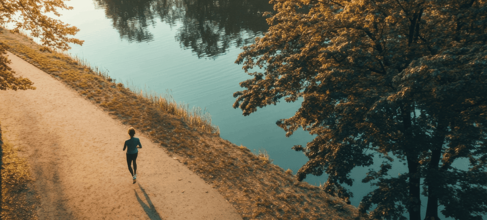 A woman running along side a body of water in the morning sunlight