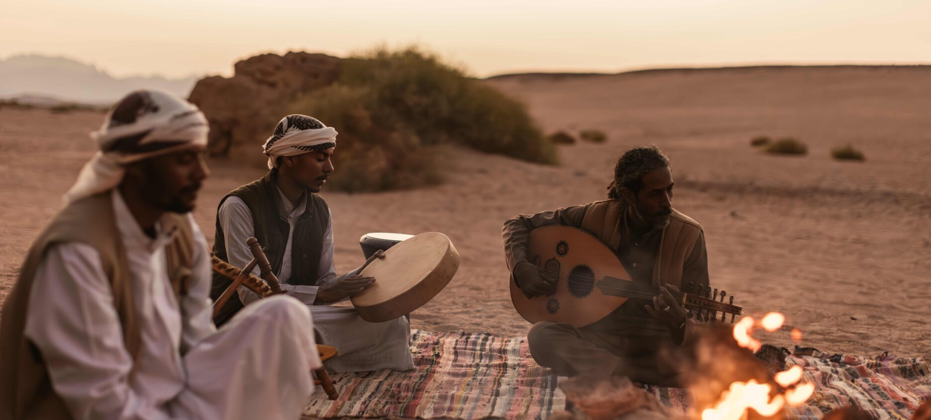 Tour guides setting up a seated area sitting around a fire, playing music as part of the dessert experience