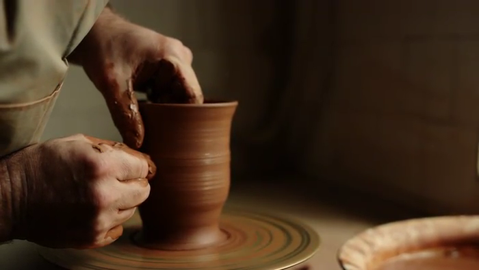 Two hands working on a piece of clay, turning it into a vase shape